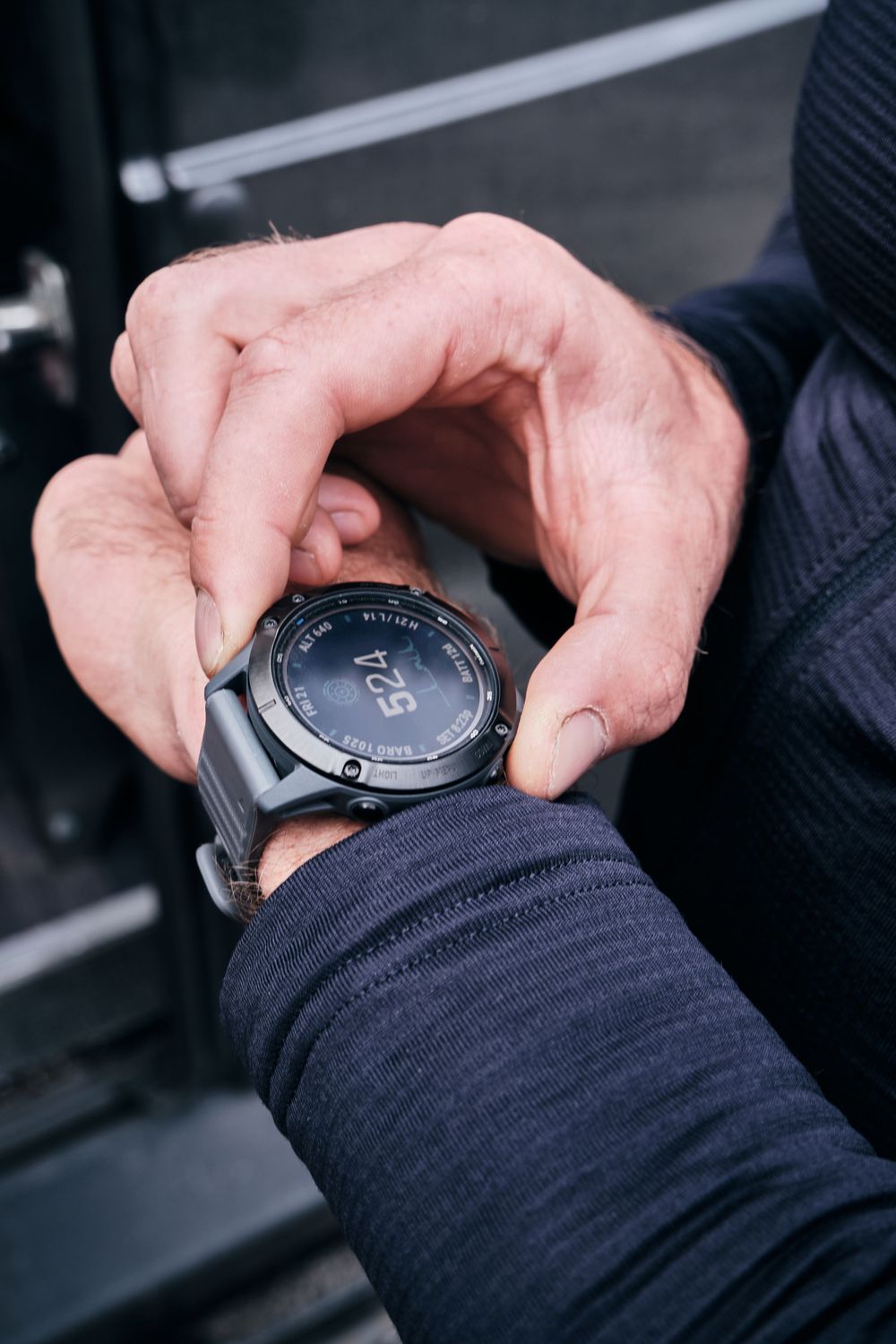 Close-up of hands adjusting a dark Garmin smartwatch on a wrist, worn by a person in a navy blue sleeve.