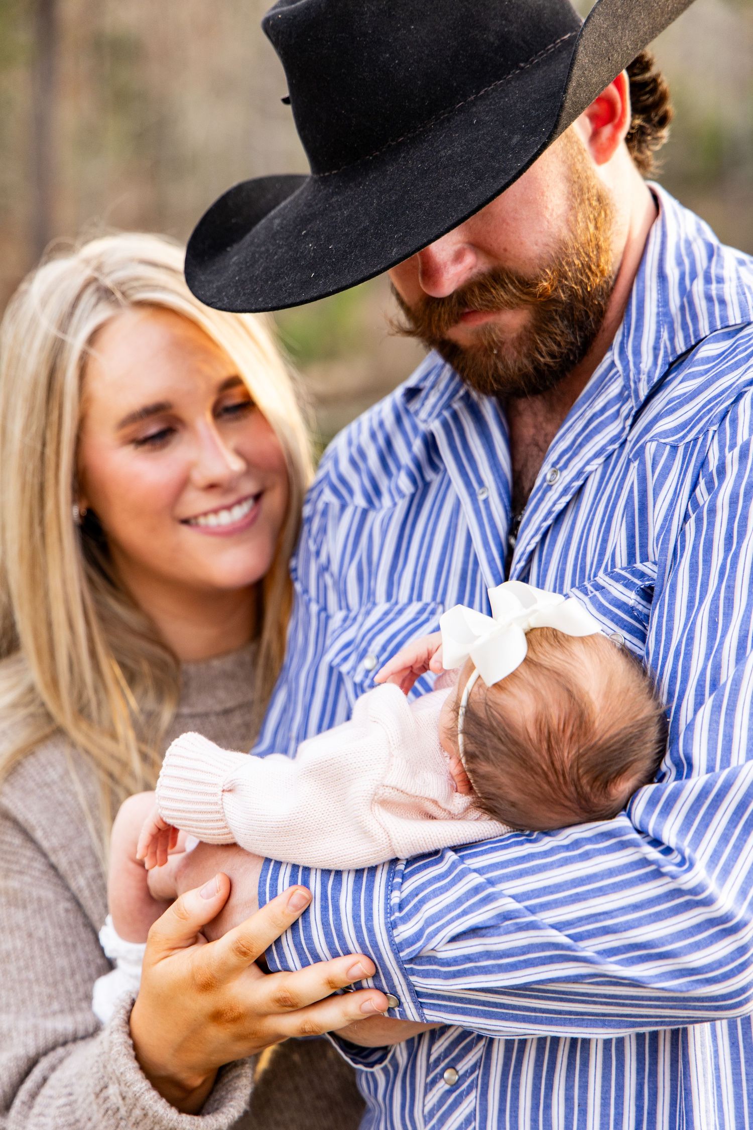 Couple in Western wear sharing a tender maternity moment outdoors, man in cowboy hat cradling pregnant woman's belly.