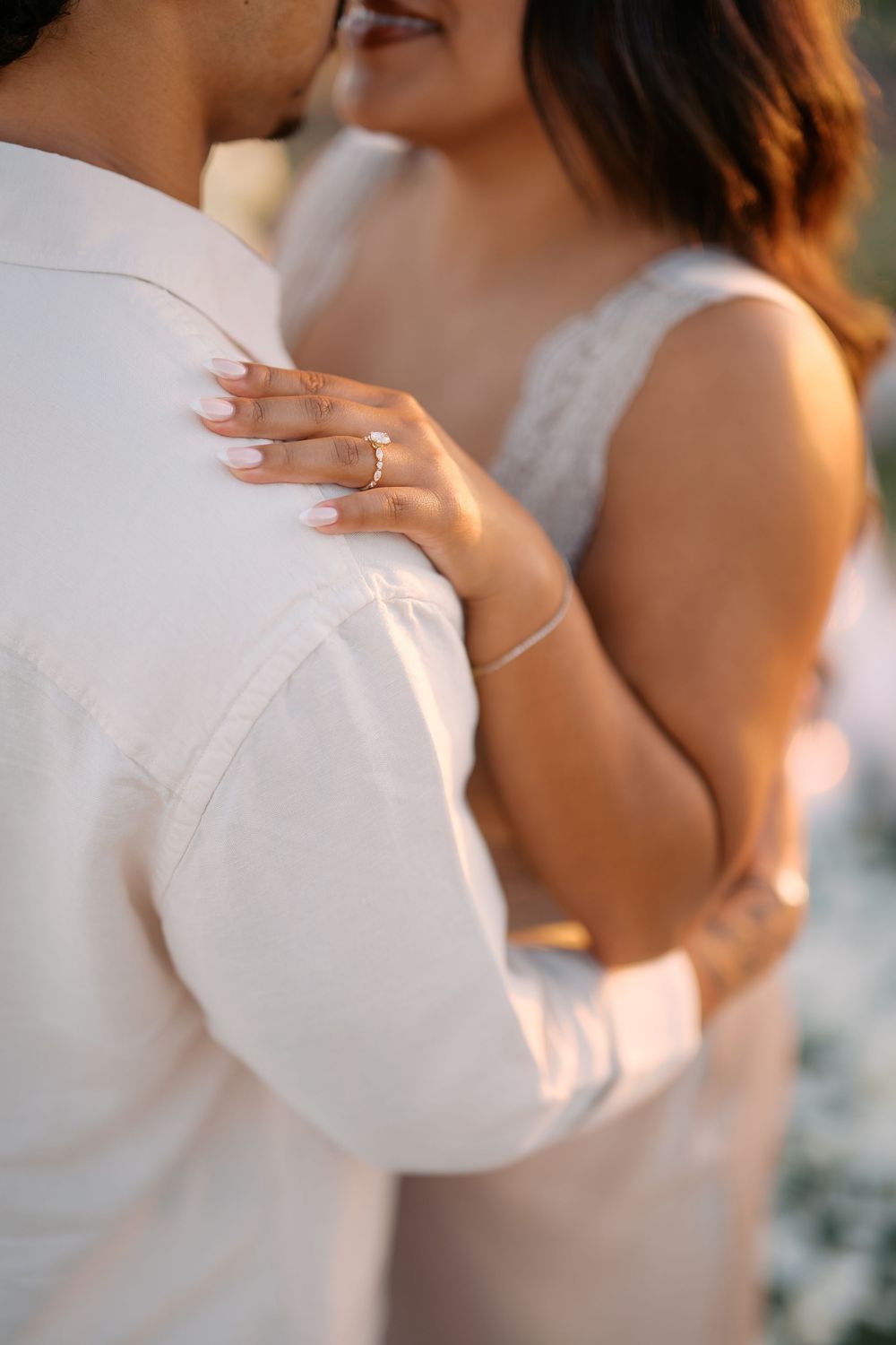 Bride and groom embracing closely, showcasing a diamond engagement ring and bracelet on the bride's hand.