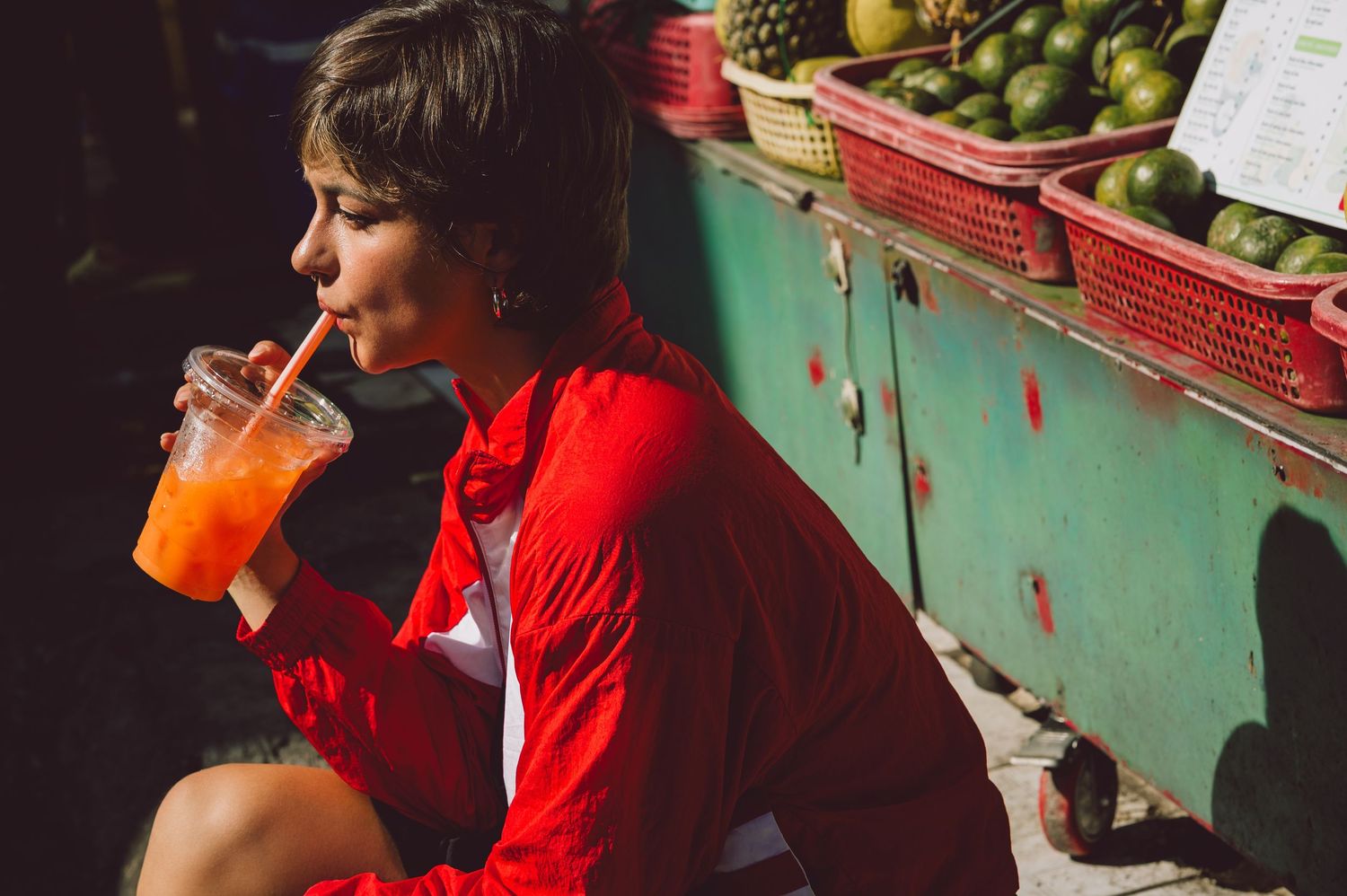 Model drinking fresh orange juice at a fruit stall in Saigon — candid editorial portrait photography by Anastasia Sokyrka