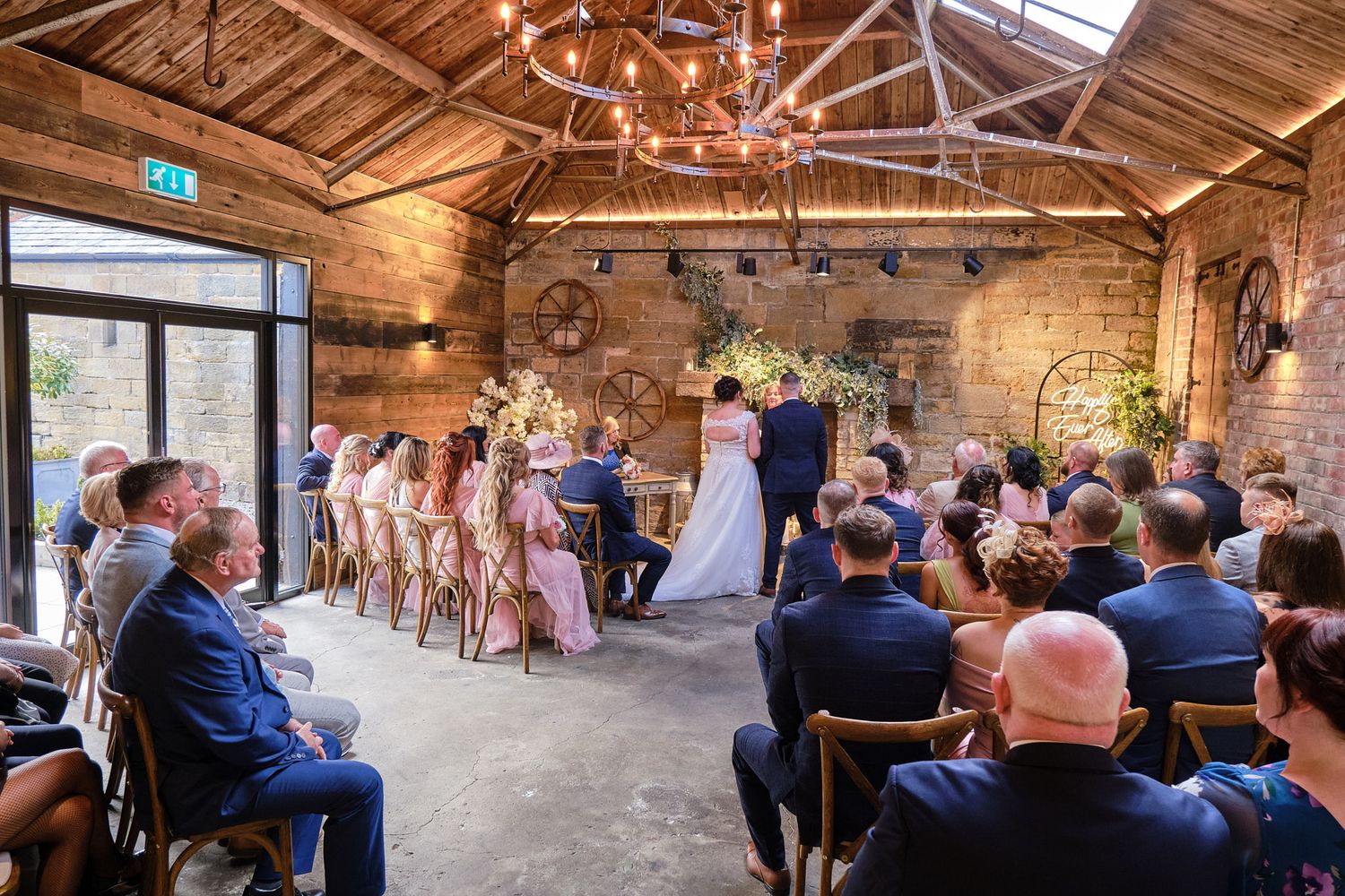 Elegant rustic barn wedding ceremony with guests seated as couple exchanges vows under warm lighting.