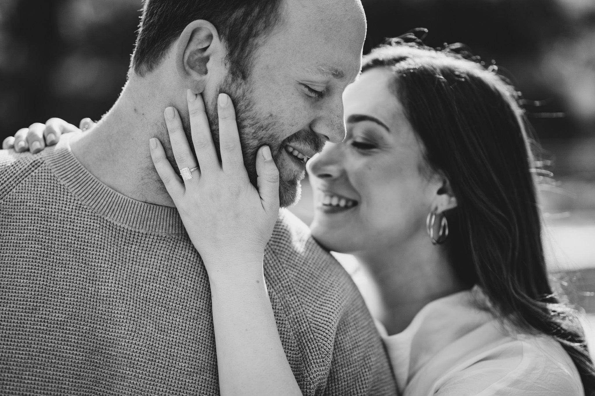 Black and white photo of a smiling couple sharing a tender, romantic moment, the woman gently holding the man's face.