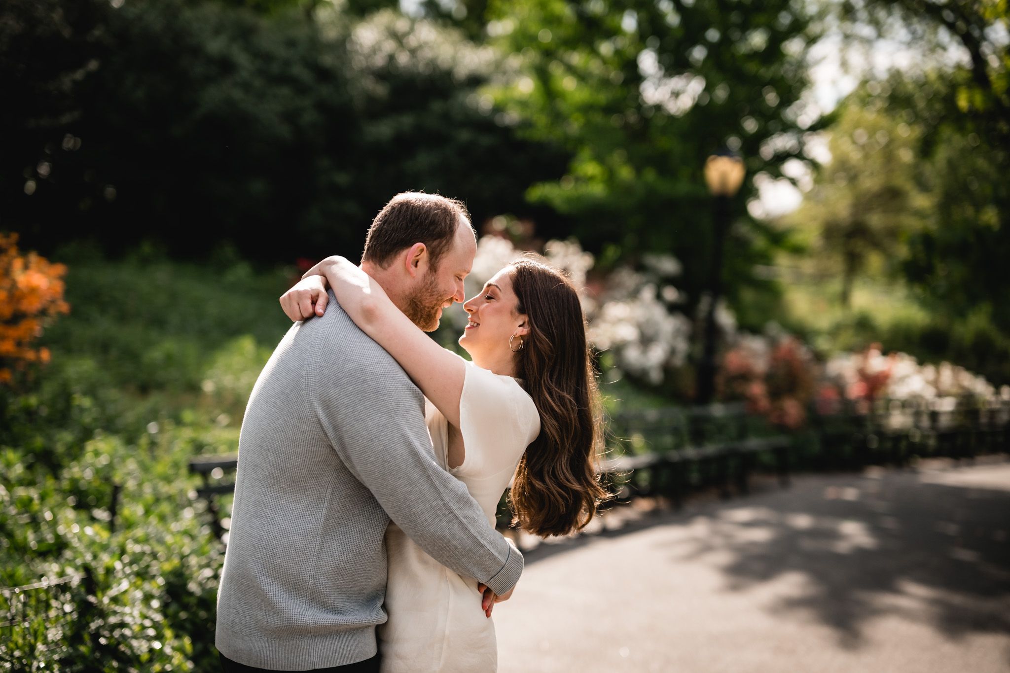 Romantic couple sharing a tender embrace on a sunlit park path surrounded by greenery.