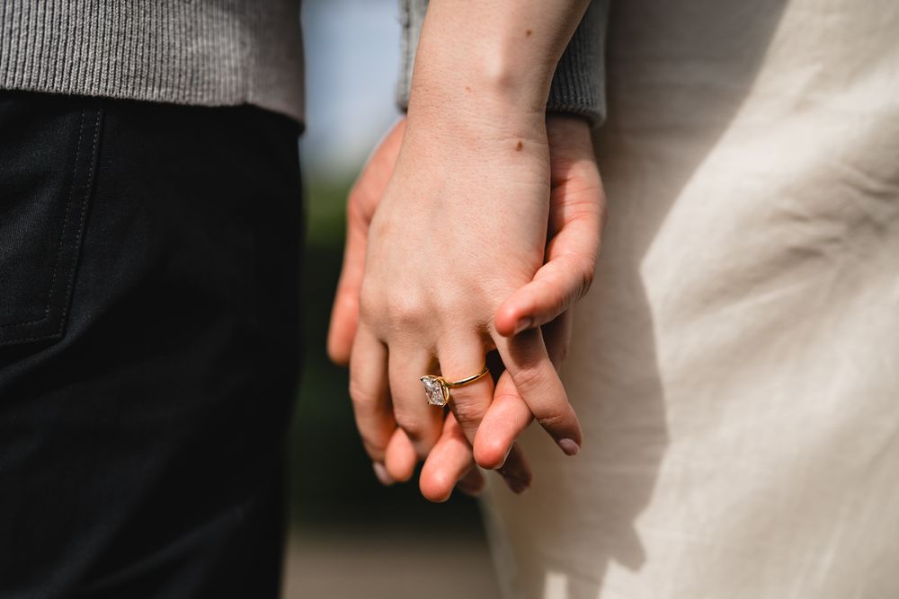 Close-up of couple holding hands showing elegant engagement and wedding rings outdoors.