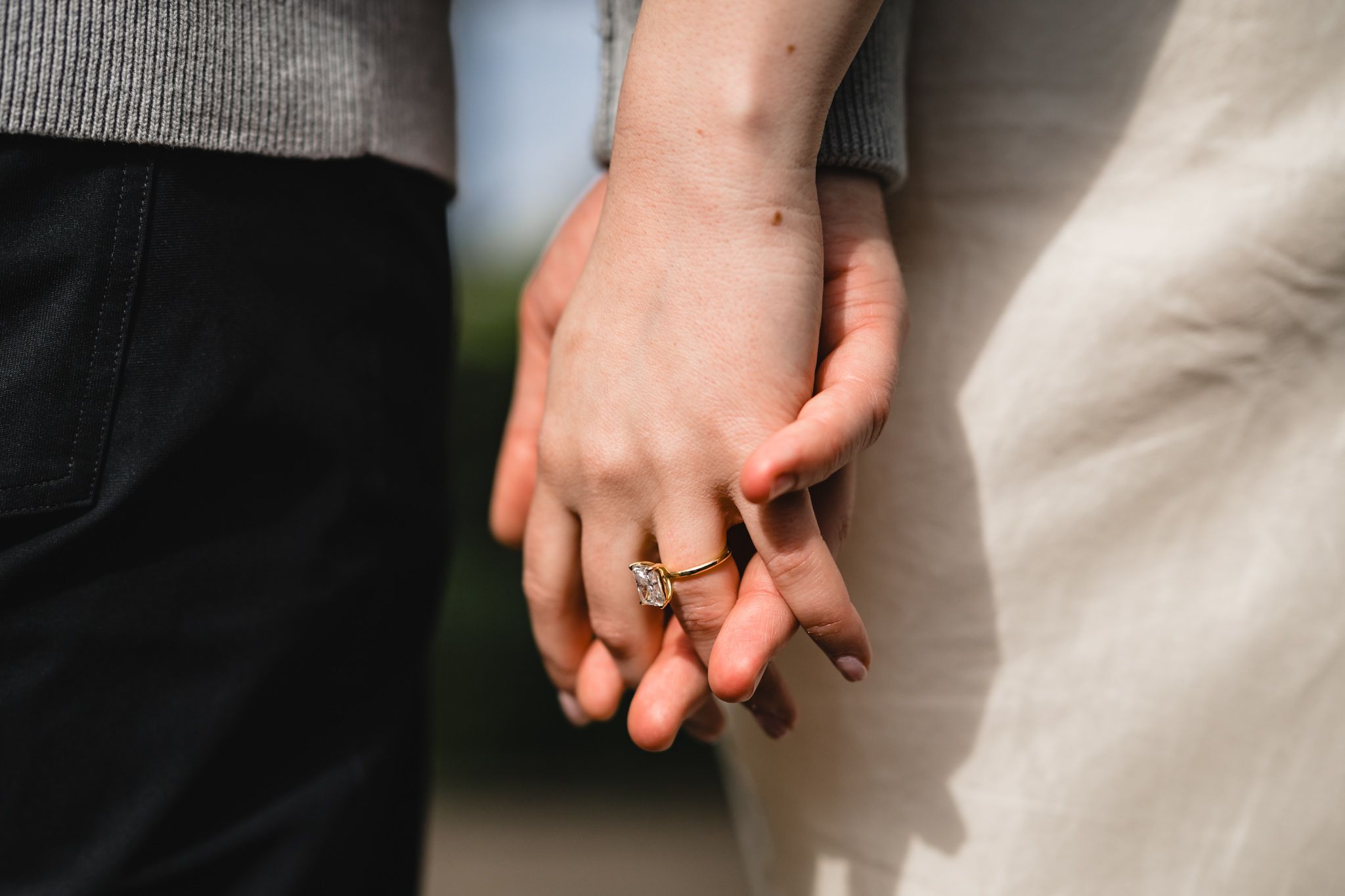 Close-up of couple holding hands showing elegant engagement and wedding rings outdoors.