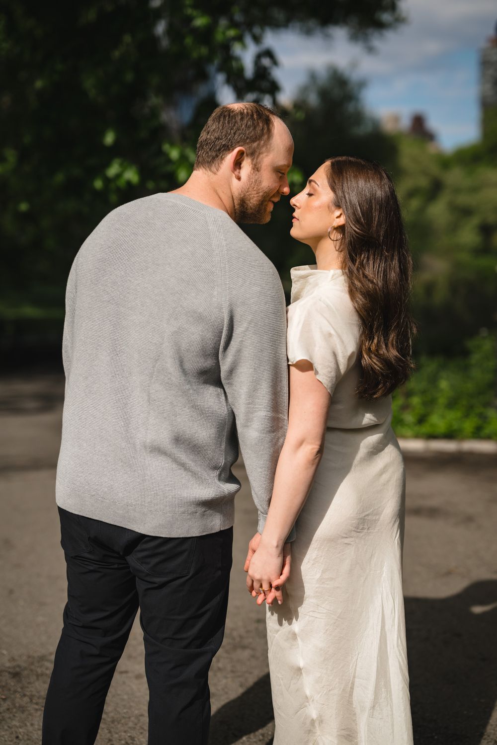 Couple holding hands and sharing a romantic moment outdoors, woman in white dress and man in gray sweater.