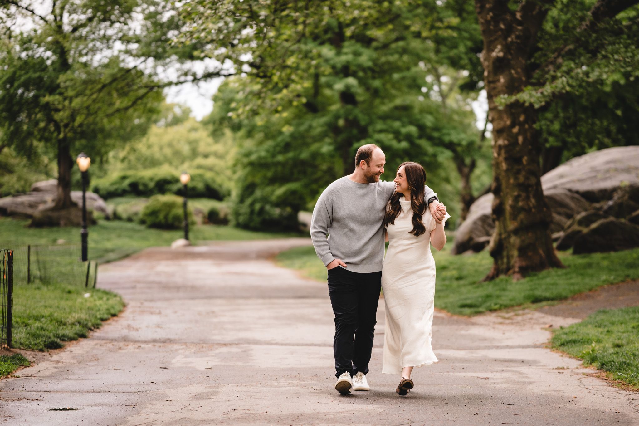 Couple walking hand-in-hand on a tree-lined path in Central Park, sharing a romantic moment outdoors.