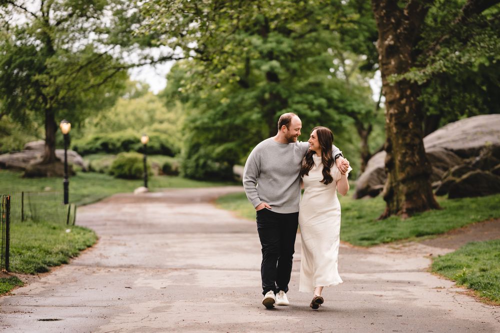 Couple walking hand-in-hand on a tree-lined path in Central Park, sharing a romantic moment outdoors.
