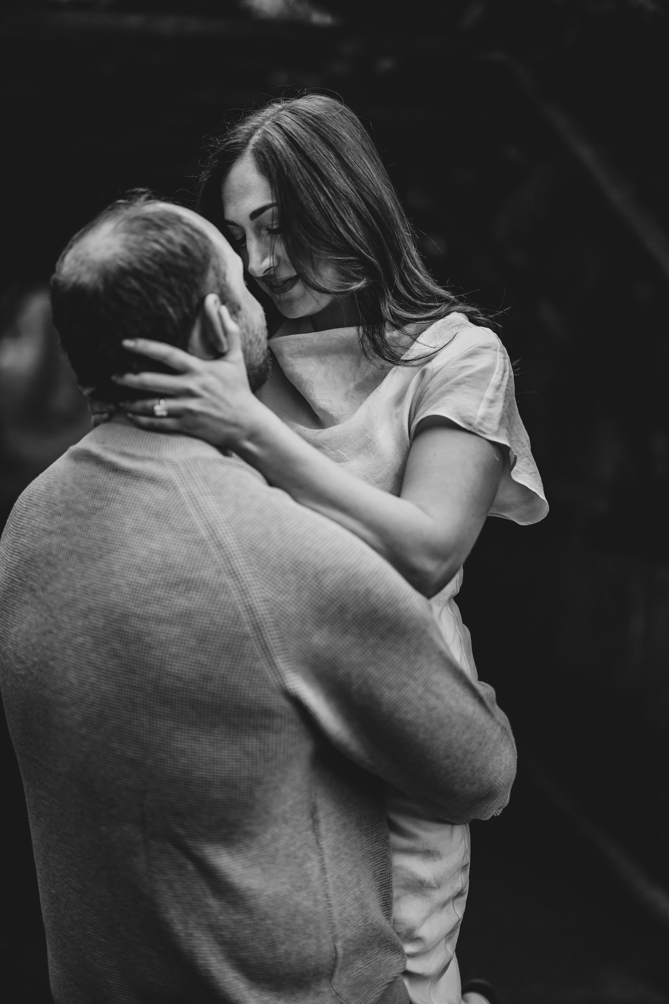 Black and white photo of a couple embracing tenderly, woman cradling mans face in an intimate moment.
