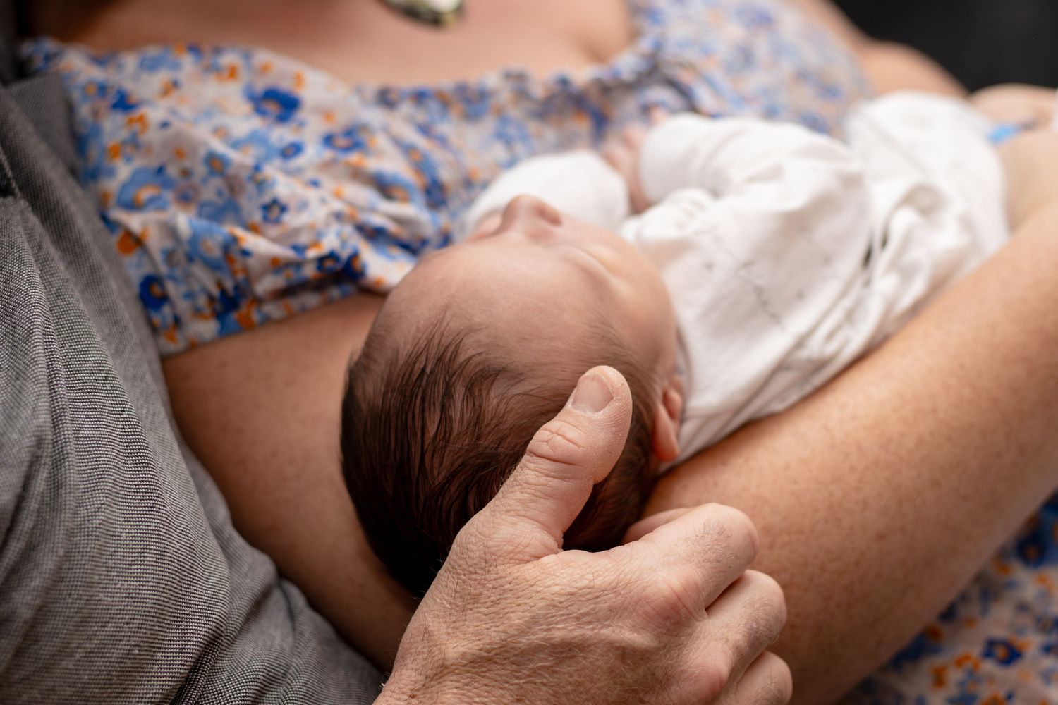 A newborn baby being cradled by a mother in a floral top, supported by a second person's hand.