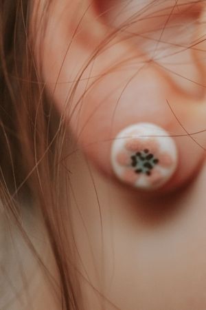 Close-up of a round floral stud earring worn on a person's ear, featuring a delicate flower design.