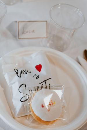 Wedding favor bag reading Love is Sweet with a frosted donut on a white plate at a reception table.