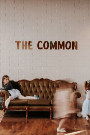 Children playing near a vintage tufted sofa beneath The Common sign on a white brick wall.