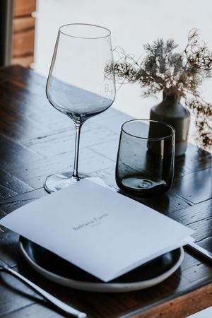 Elegant table setting with wine glass, menu, dark plate, and floral vase at Bellana Farm restaurant.