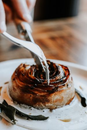 Close-up of a caramelized onion tart on a white plate being cut with a knife, garnished with sage leaves.