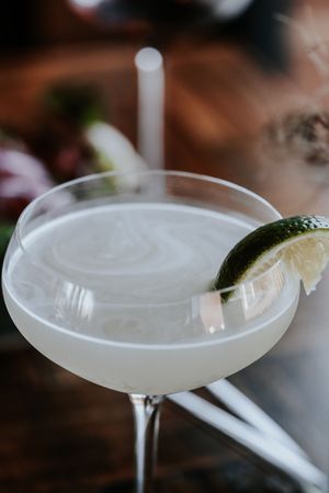 A frosted coupe glass with a lime wedge garnish, filled with a milky white cocktail, set on a dark bar.