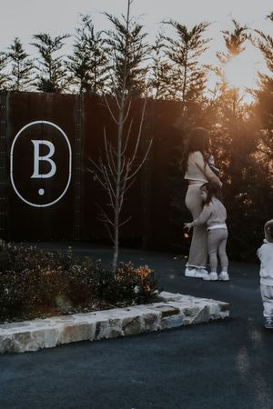 Family silhouetted at golden hour near a wooden fence with letter B sign, surrounded by trees and landscaping.