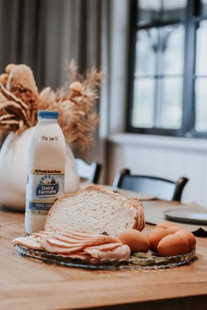 Dairy Farmers full cream milk bottle beside sliced bread, ham, and brown eggs on a wooden table.