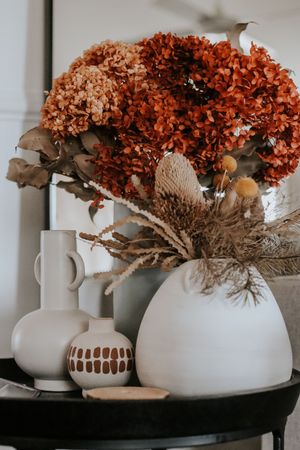 Autumn dried hydrangea arrangement in white ceramic vases on black table with warm rust tones.