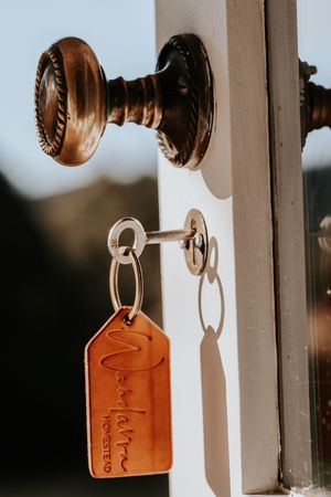 A brass door knob with a key inserted, featuring a leather keychain tag reading Marvelous Homestead.