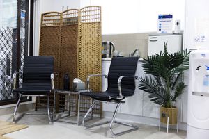 Modern black office waiting area chairs with chrome legs arranged in a row beside a decorative wicker screen and tropical plant.