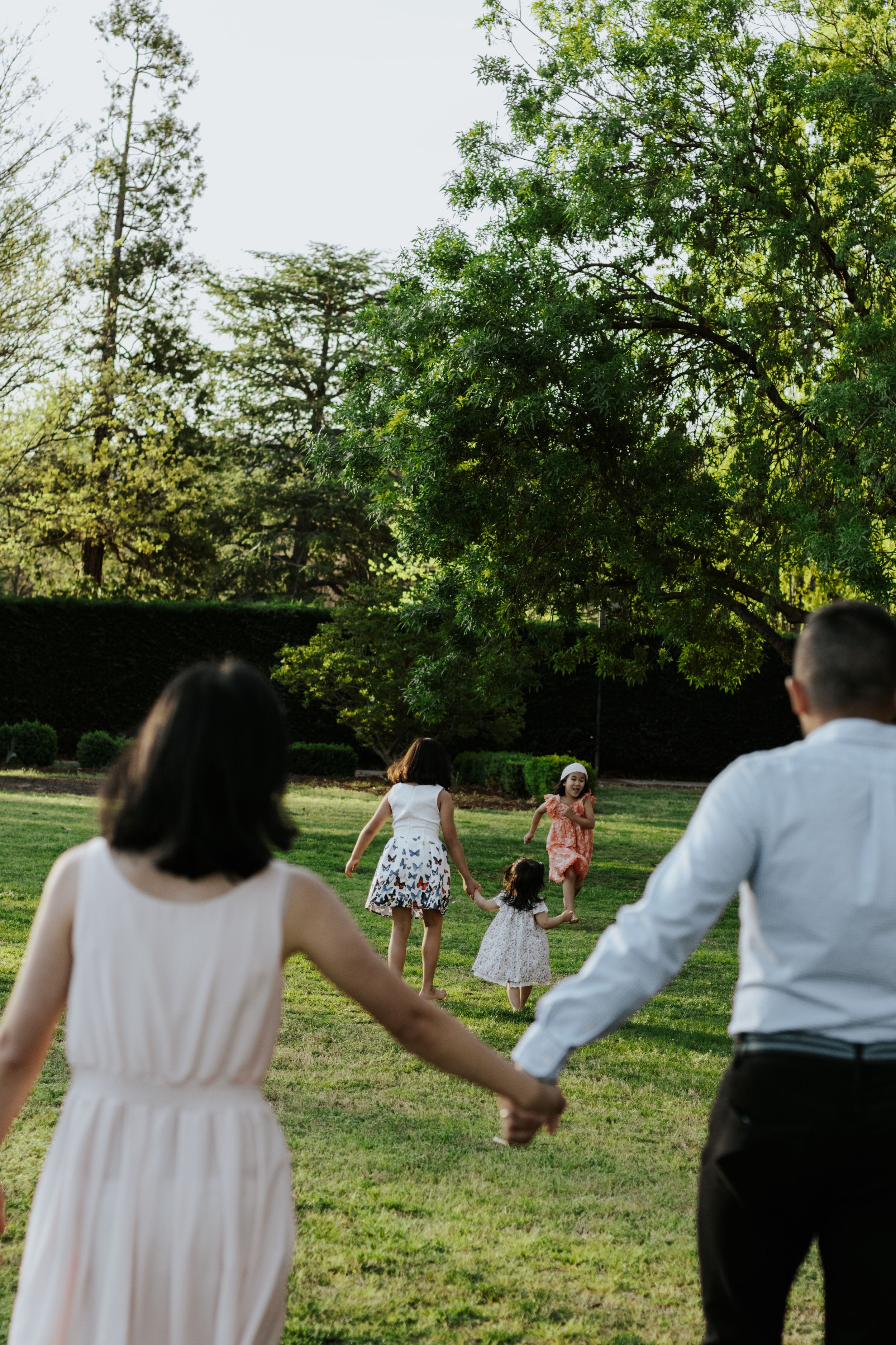 Family holding hands walking toward children playing in a lush green park on a sunny day.