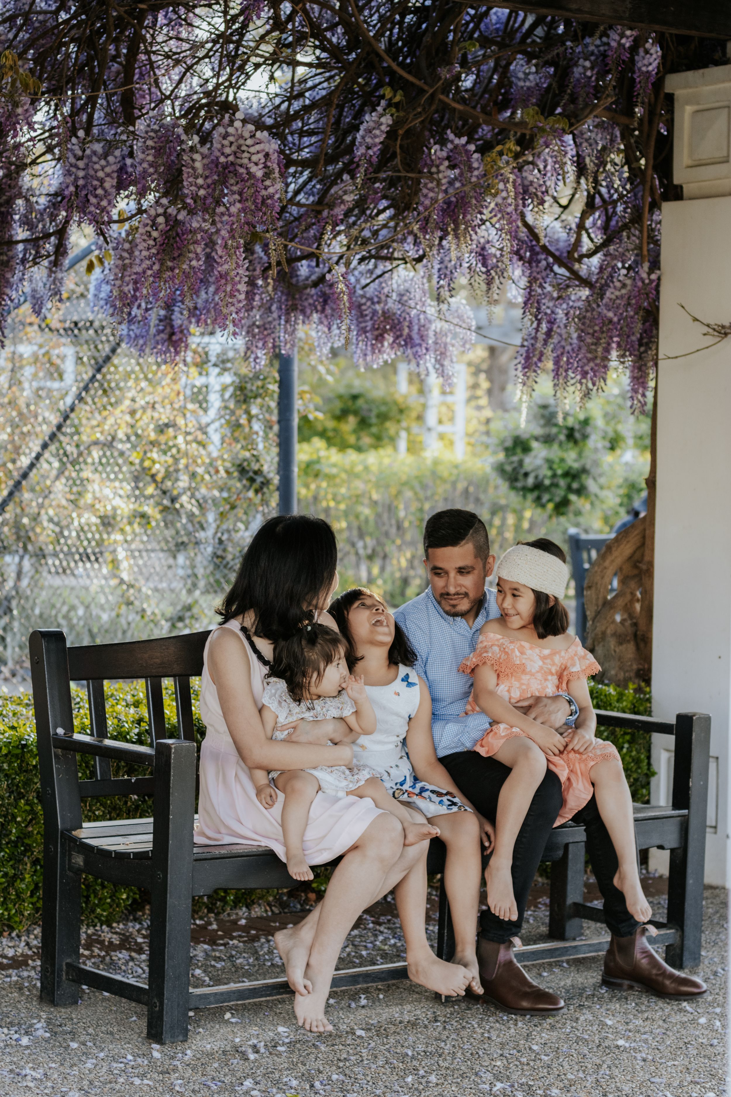 Family of four sitting on a bench under blooming wisteria, sharing a tender moment outdoors.