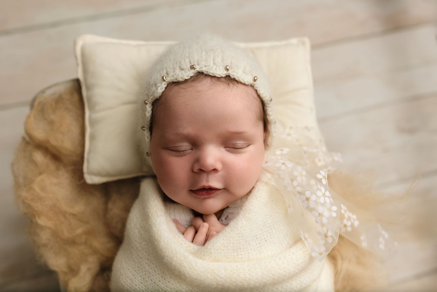 Smiling newborn girl wrapped in white knits and lace cap sleeps during her session at Charlottesville photography studio.