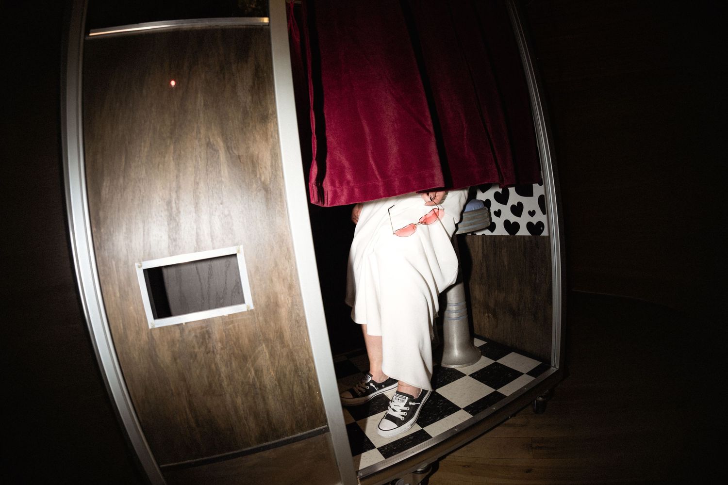 Guests gather near a photo booth and bar area at a dimly lit event venue with exposed brick walls.