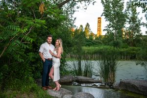 Elegant couple posing on rocks beside a peaceful pond surrounded by lush green trees at sunset.