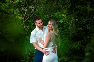 Couple embracing romantically among vibrant green tropical foliage with warm soft natural lighting.