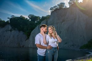 Couple laughing and enjoying a moment together near a scenic rocky cliff beside a calm blue lake.