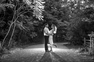 A couple dances joyfully on a forest path in this romantic black and white engagement photo.