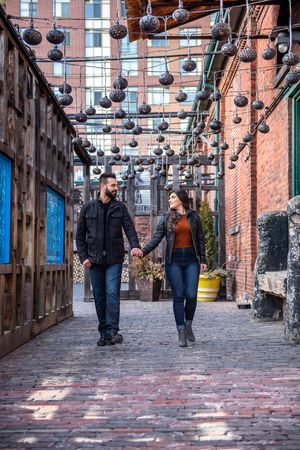 Couple holding hands and walking through a charming alley with decorative hanging lanterns.