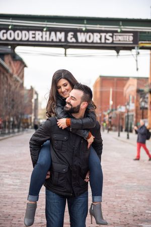 Happy couple laughing as man gives woman a piggyback ride under Gooderham and Worts sign.