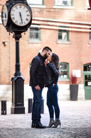 Couple sharing a kiss near a vintage street clock in a charming cobblestone district.
