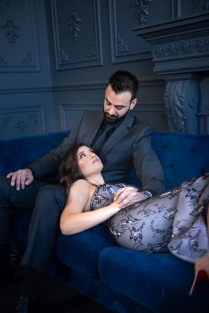 Couple in formal wear sharing an intimate moment on a blue velvet sofa in an elegant room.