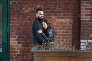 Romantic couple embracing against a rustic red brick wall in an outdoor urban setting.