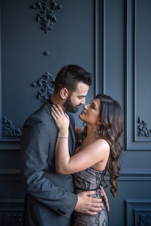 Couple in formal wear sharing a romantic moment against an ornate dark grey decorative wall.