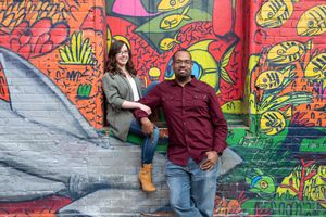 Smiling couple posing together in front of a colorful fish and nature graffiti mural on a brick wall in Graffity Alley in Toronto..