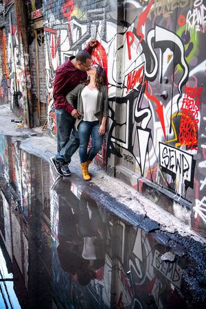 Couple kissing beside a graffiti wall reflected in a puddle on a wet urban alleyway in Graffity Alley in Toronto.