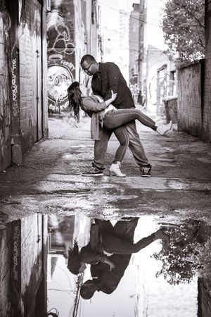 A couple shares a dramatic dip pose reflected in a rain puddle in a graffiti-covered urban alley in Graffity Alley in Toronto..