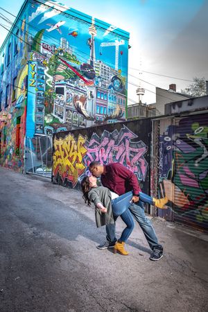 Couple sharing a romantic dip kiss in front of a vibrant Toronto cityscape graffiti mural in Graffity Alley in Toronto.