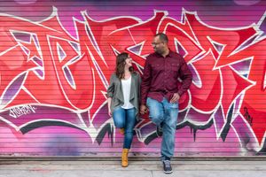 Couple holding hands and smiling at each other against a bright pink and red graffiti wall in Graffity Alley in Toronto.