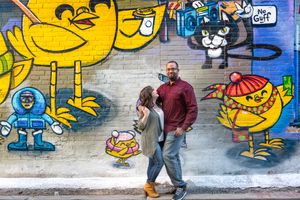 Couple embracing while walking past a colorful cartoon characters graffiti mural on a city wall in Graffity Alley in Toronto.