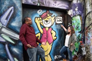 Couple pointing and laughing at a Yogi Bear graffiti mural saying Chill Dude on an urban wall in Graffity Alley in Toronto..