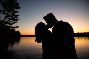 Romantic silhouette of a couple kissing by a lake during a stunning colorful sunset.