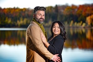 Couple posing together by a lake with vibrant autumn foliage reflecting in the water.