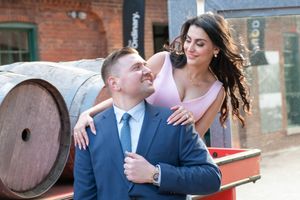 Stylish engaged couple laughing together near rustic wooden barrels at distillery district.