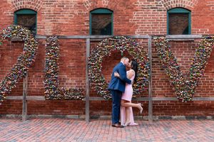 Couple sharing passionate kiss in front of love lock display spelling love on brick wall.